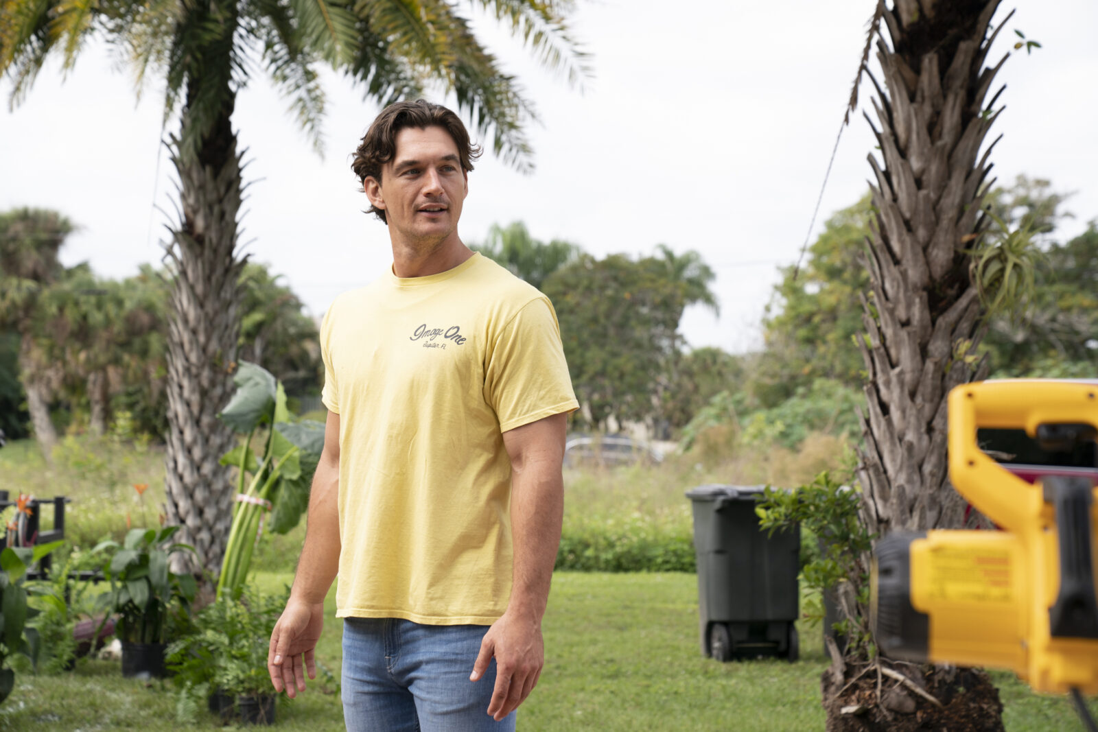 Former Bachelorette star Tyler Cameron stands in a landscape with palm trees.