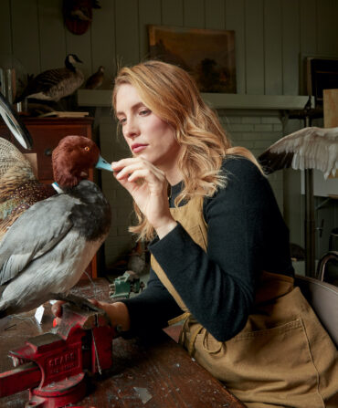 A woman sits at a desk and works on a taxidermy duck