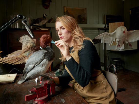A woman sits at a desk and works on a taxidermy duck