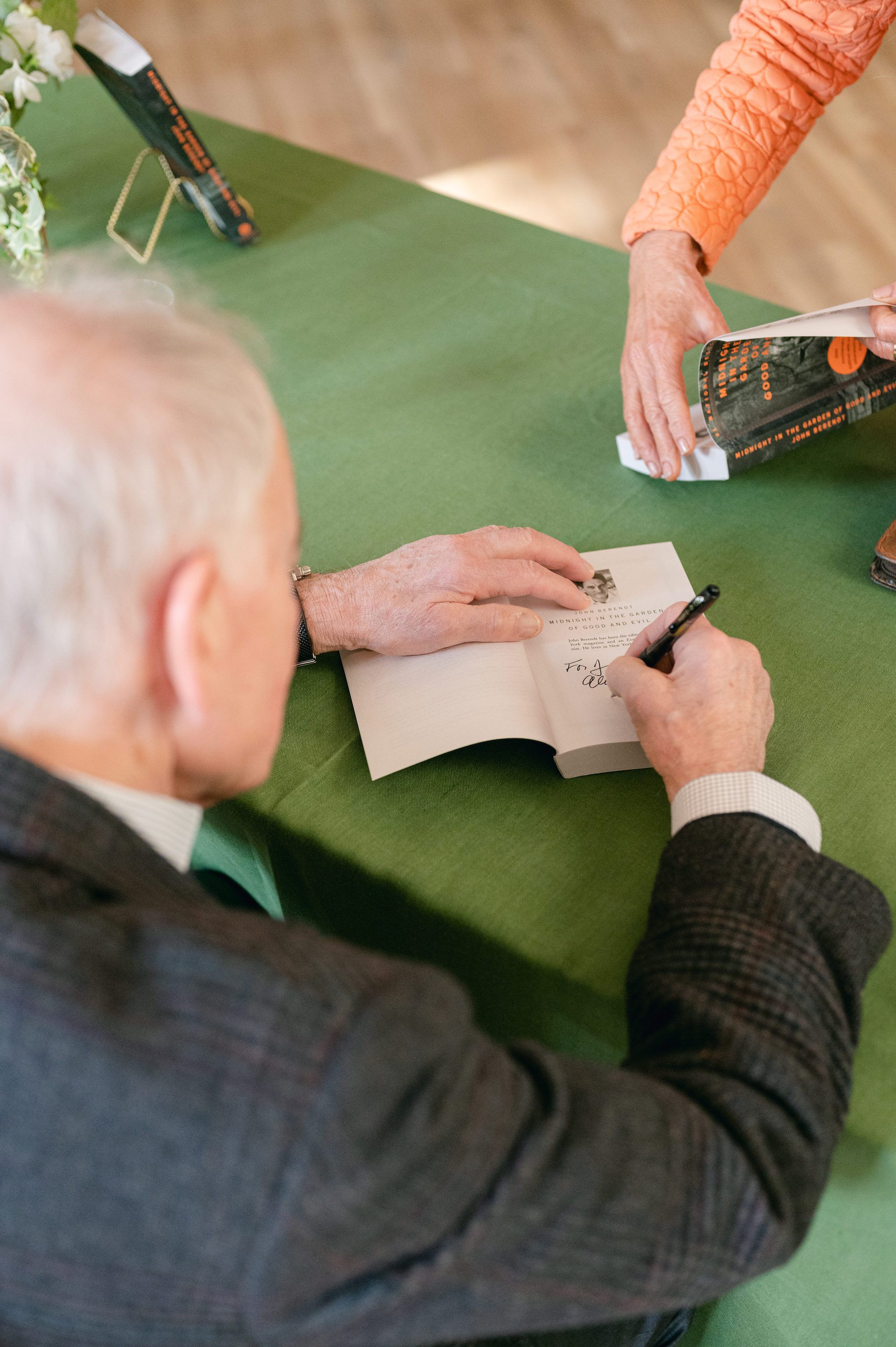A man signs a copy of a book on a green table