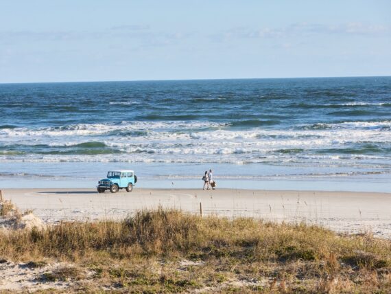 two people walking on the beach and a blue truck parked in the sand