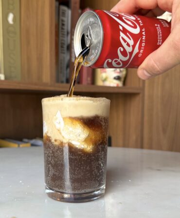 A hand pours a can of coke into a frosted glass with divinity candy