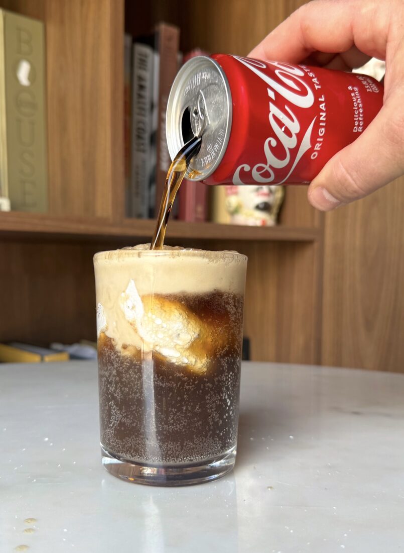 A hand pours a can of coke into a frosted glass with divinity candy