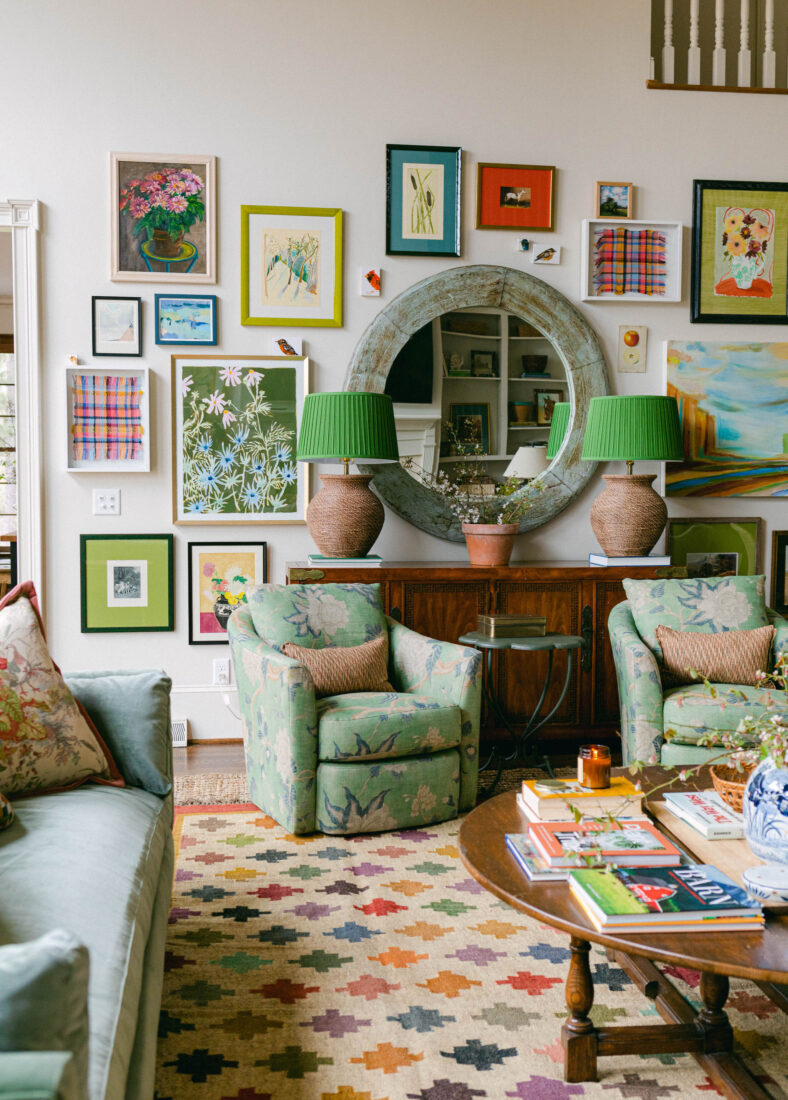 A colorful living room with many works of art on the wall, green chairs, and a patterned rug