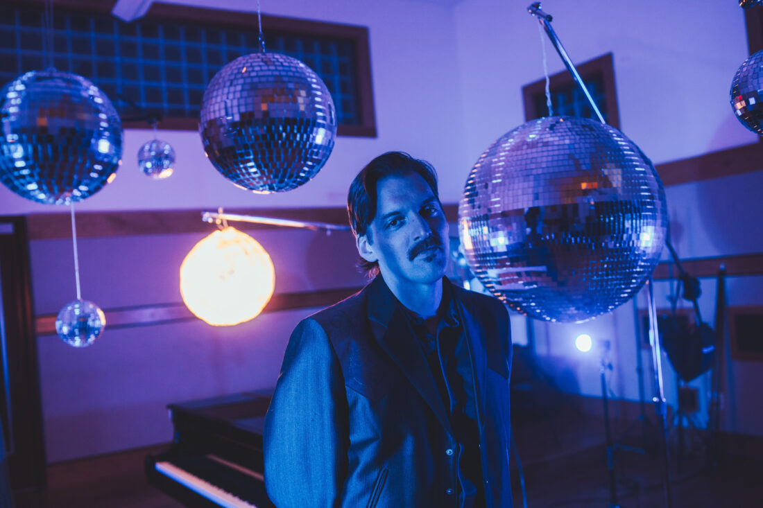 A portrait of a man in purple light surrounded by hanging disco balls