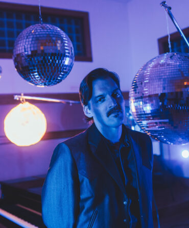 A portrait of a man in purple light surrounded by hanging disco balls