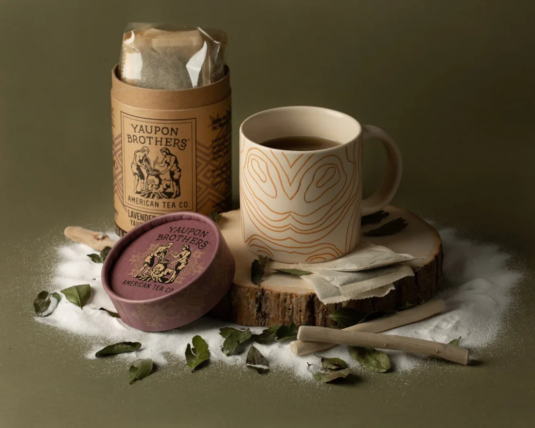 A mug with a tin of tea and some tea leaves strewn around the mug.