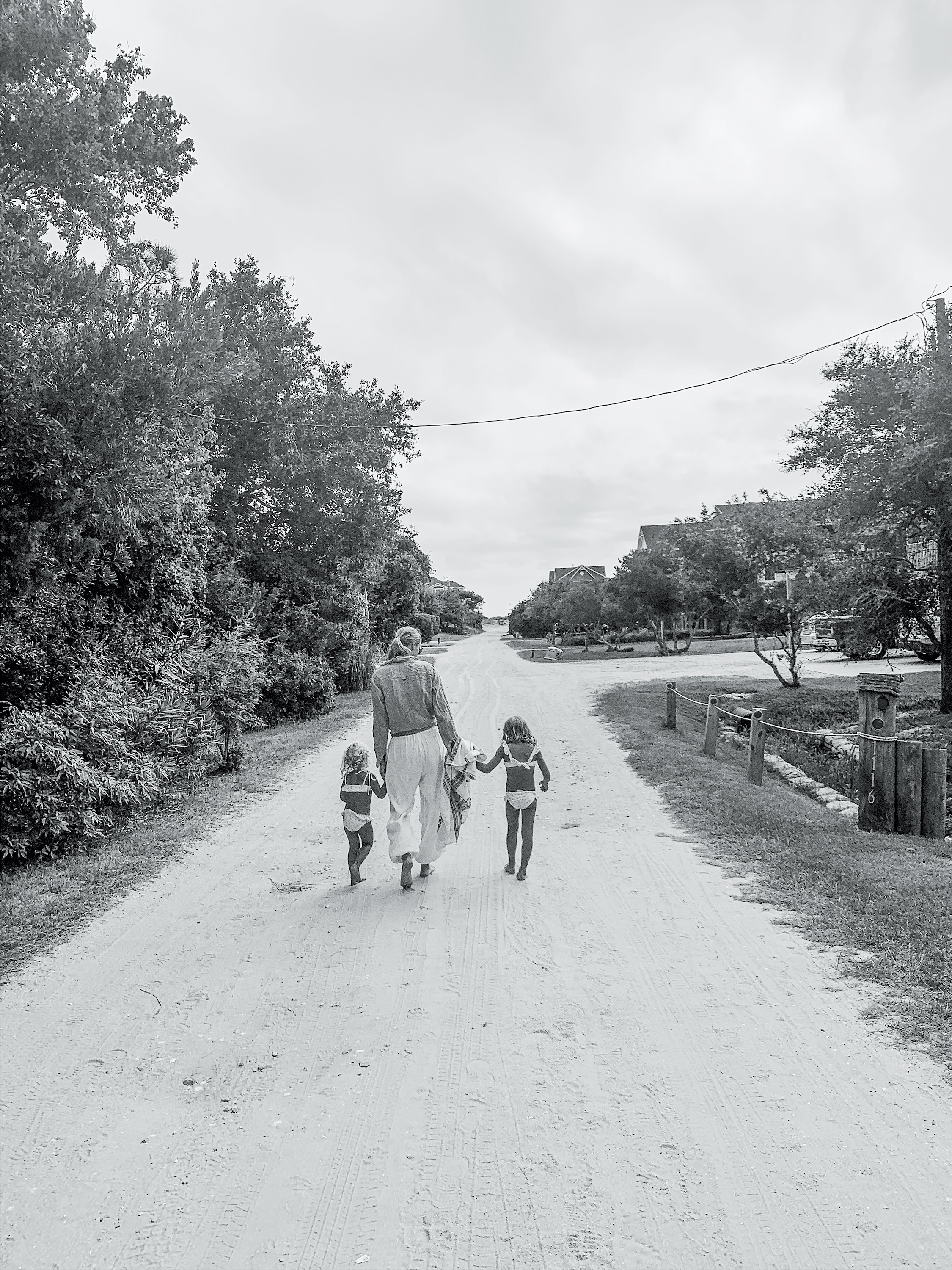 A black and white photo of a woman and two children walking on a beach path