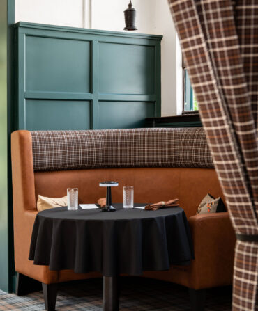 A leather booth with dark green paint details and a plaid curtain
