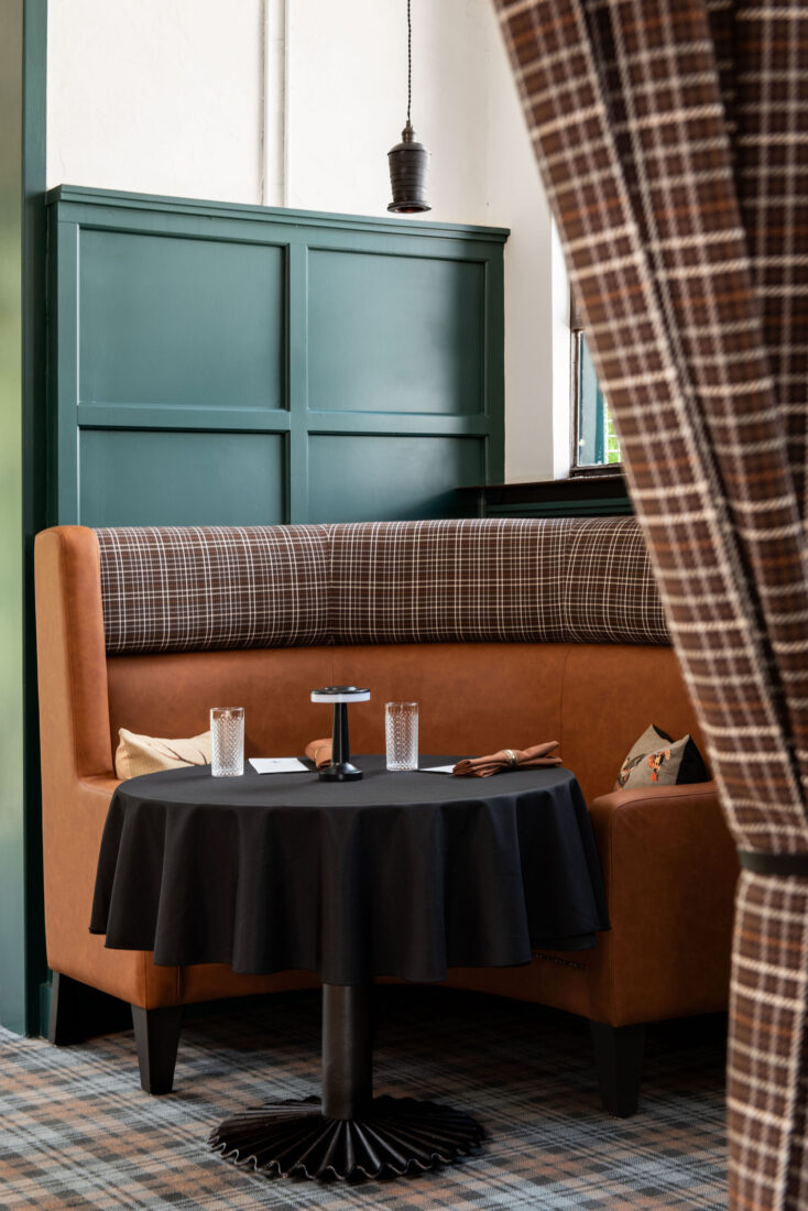 A leather booth with dark green paint details and a plaid curtain