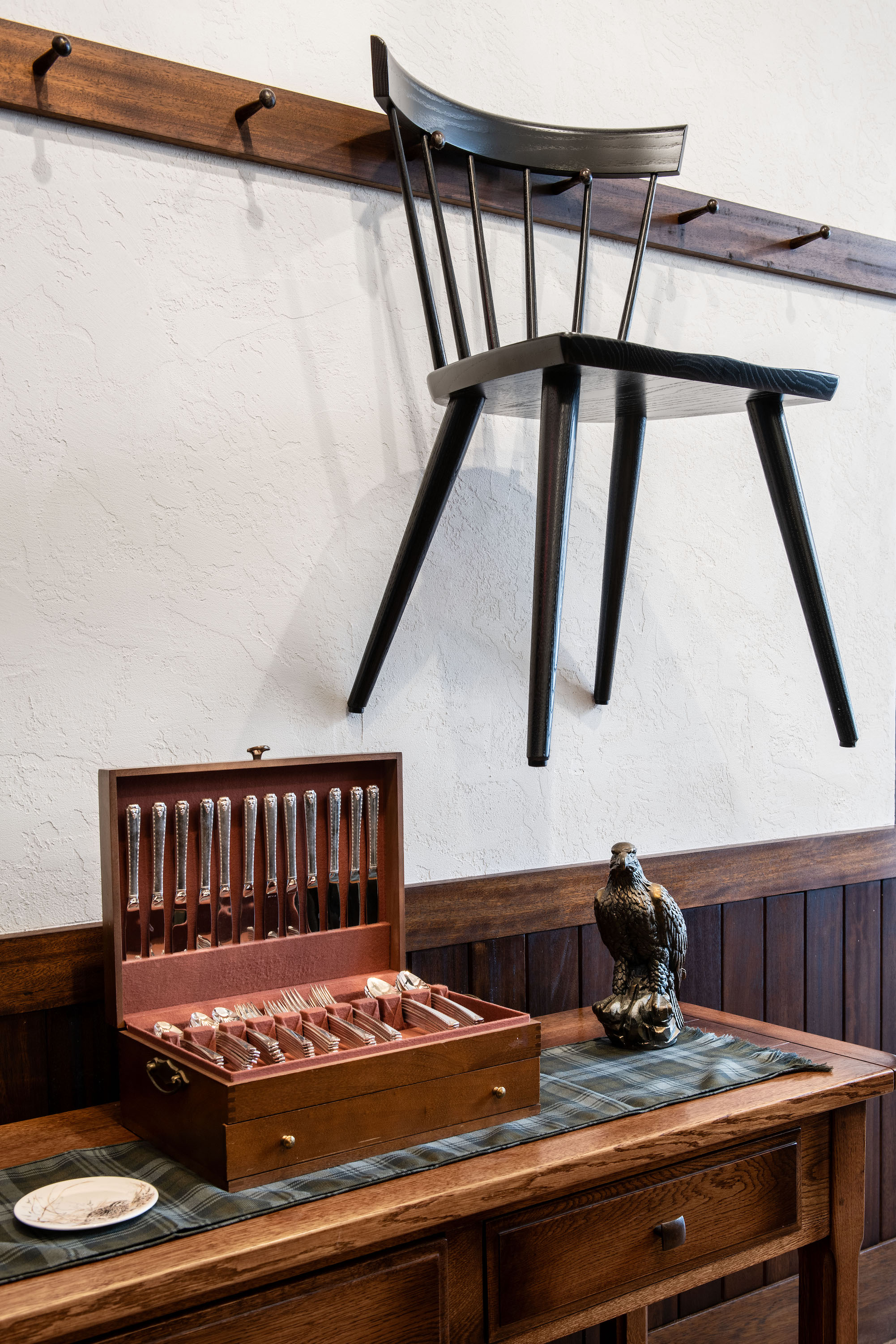 A chair hangs above a table with silverware in a box