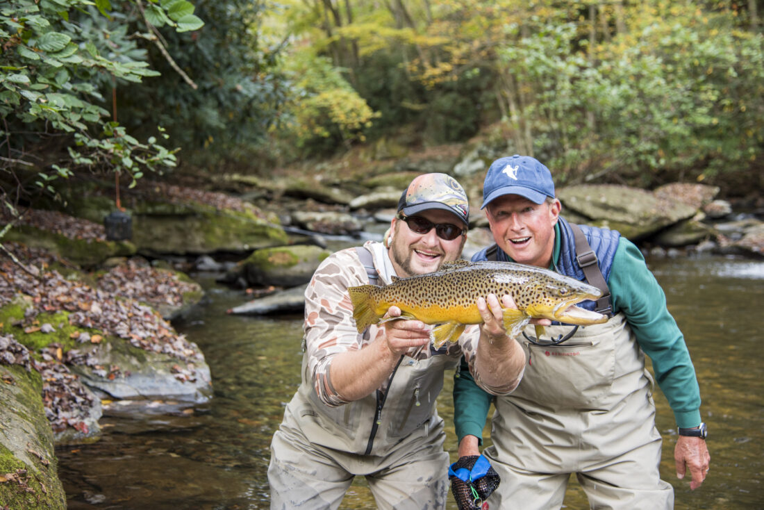 Two men pose with a fish in a stream