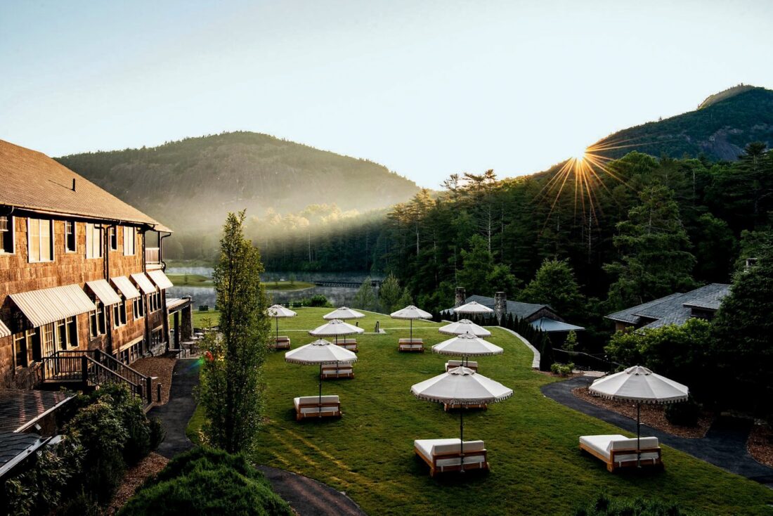 lounge chairs with umbrellas facing a mountain next to a hotel at sunrise