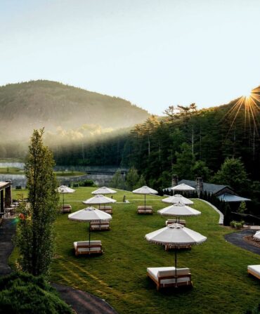 lounge chairs with umbrellas facing a mountain next to a hotel at sunrise