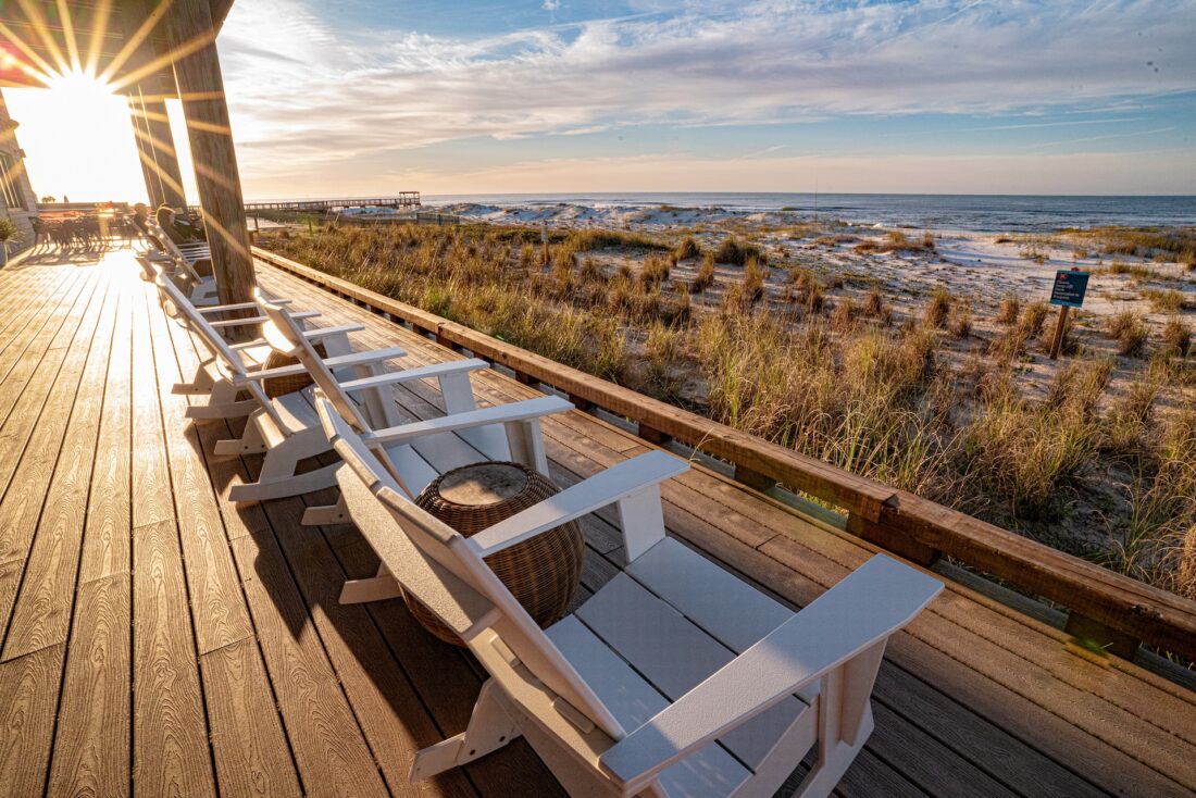 Adirondack chairs facing the ocean on a deck at sunrise