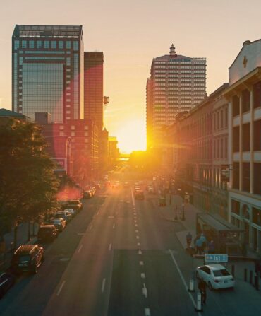 a cityscape with the sun rising over the road