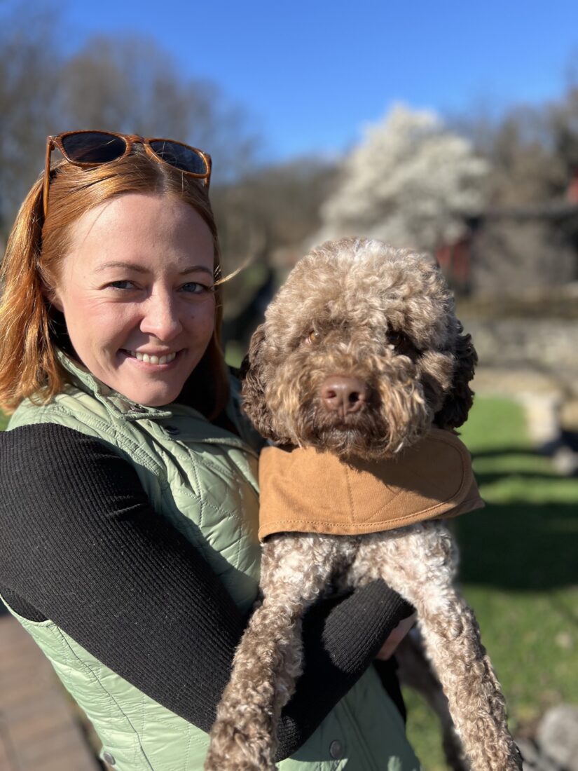 A woman holds a brown poodle dog