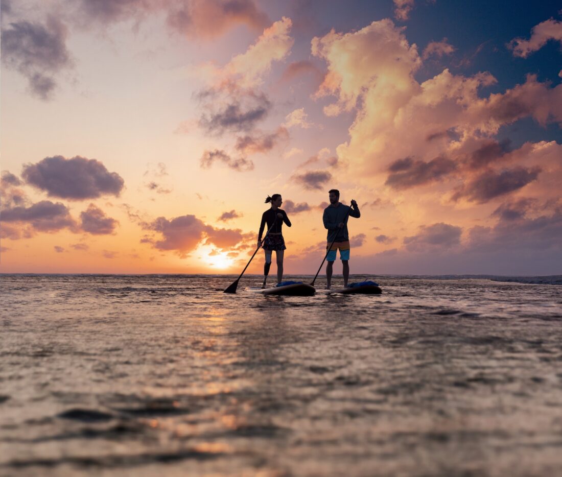 two people paddleboarding on the ocean at sunset