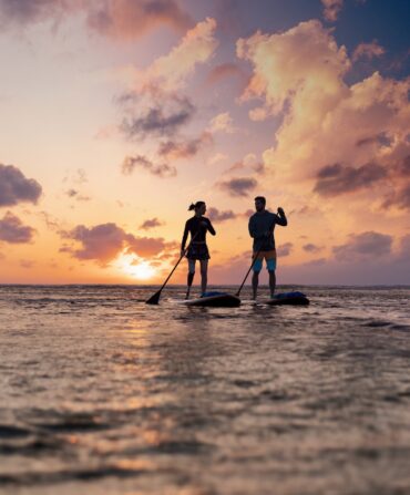 two people paddleboarding on the ocean at sunset