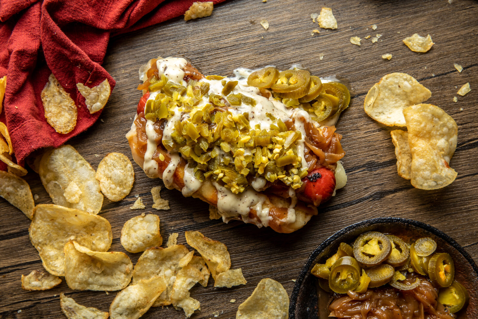A loaded hot dog on a table with potato chips
