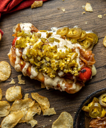 A loaded hot dog on a table with potato chips