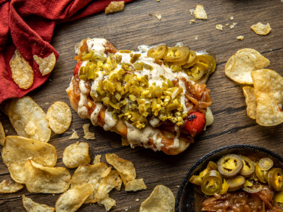 A loaded hot dog on a table with potato chips