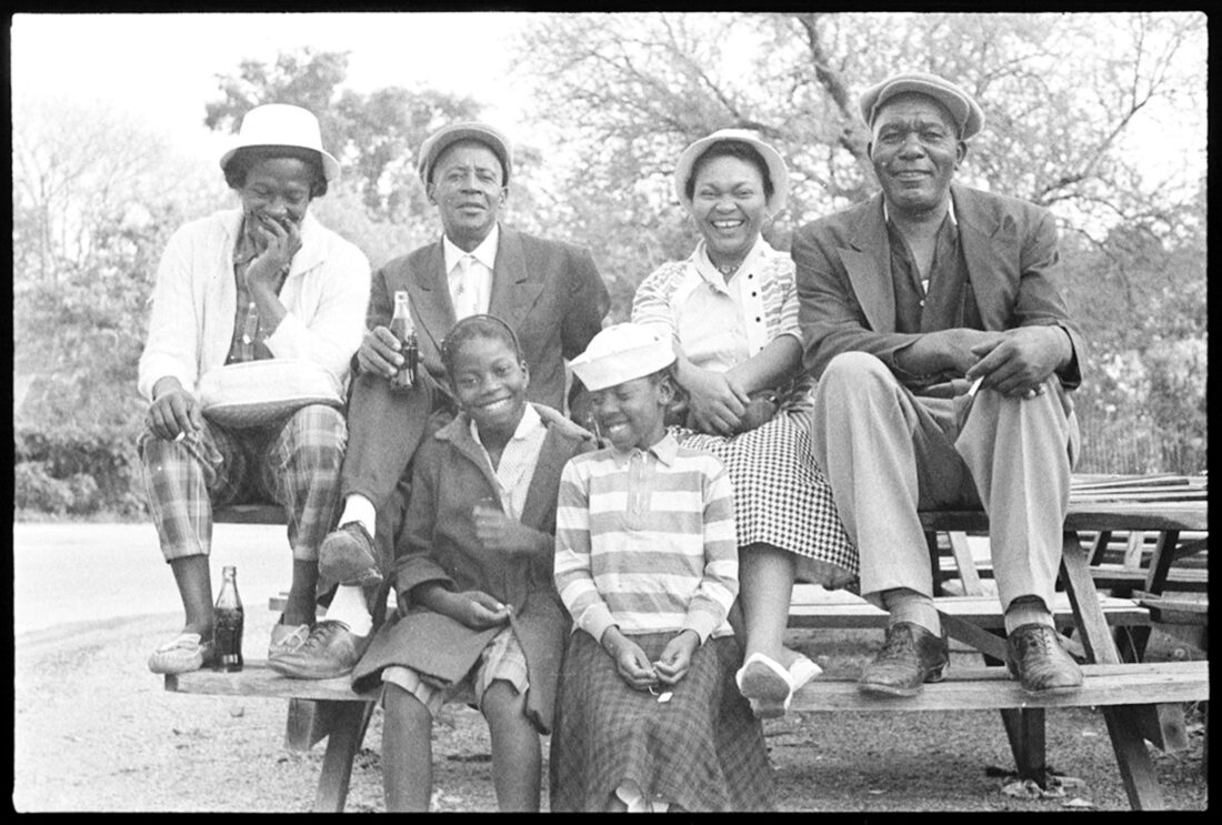 A group of people sit on a picnic table and smile