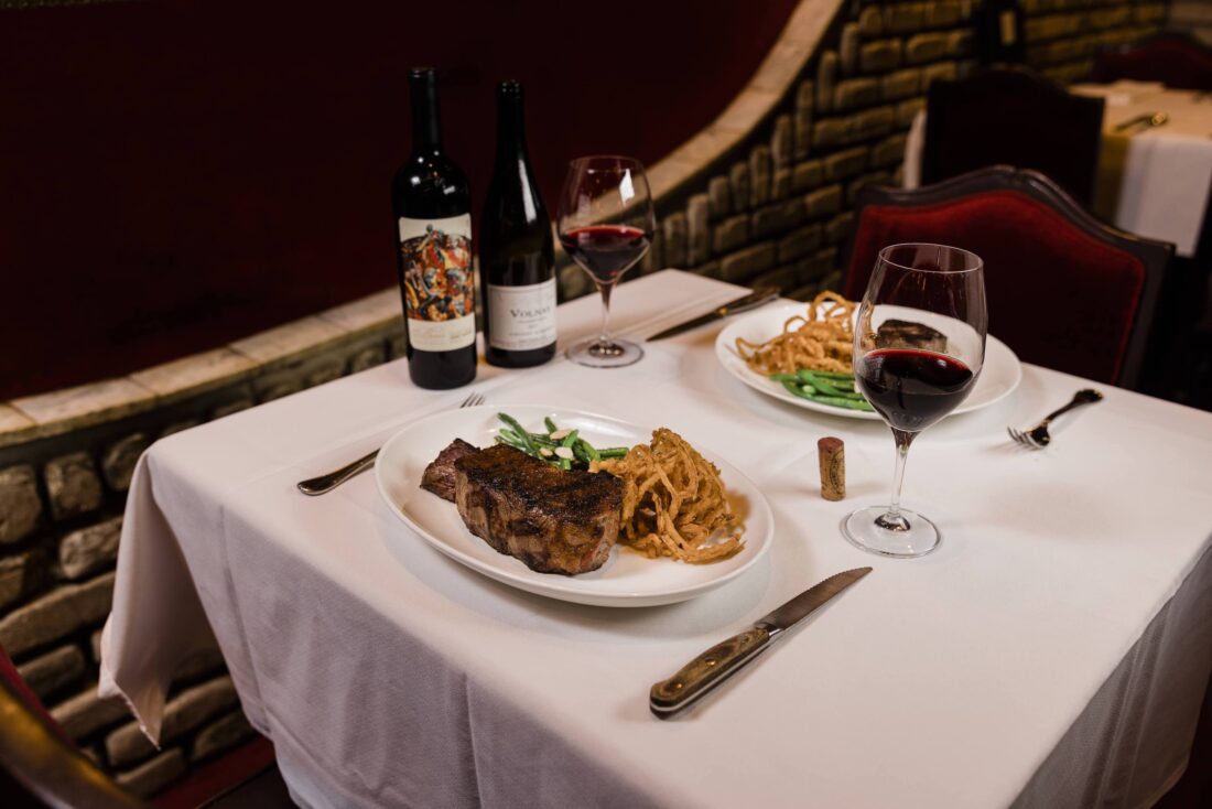 A steakhouse sets a white table with a plate of steak and sides