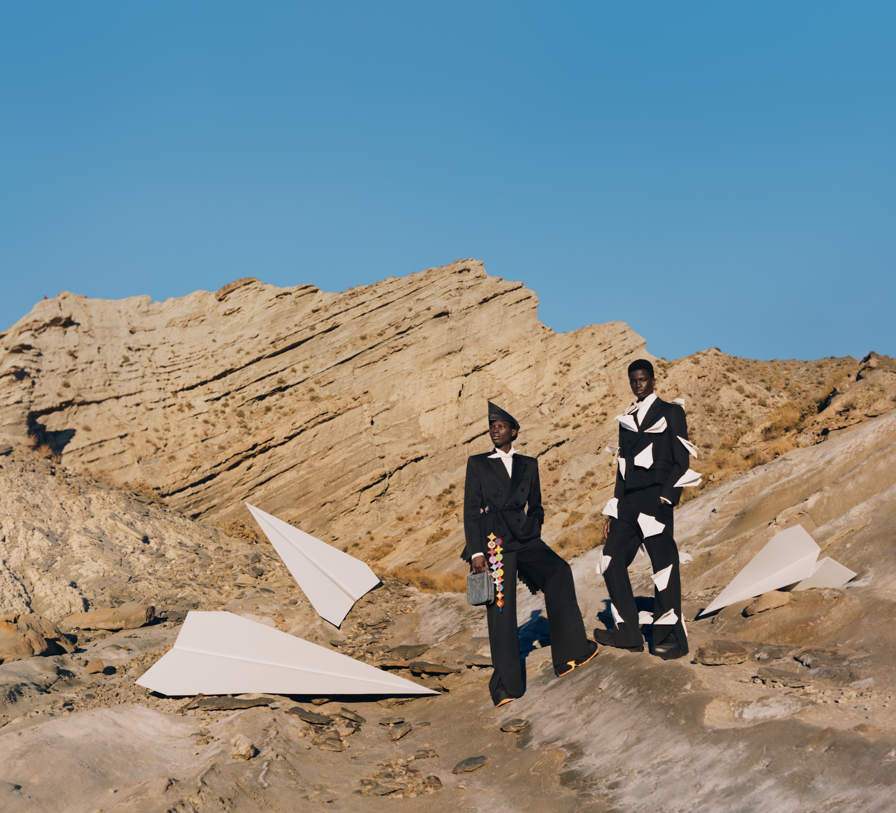 Men stand in the desert next to large paper airplanes