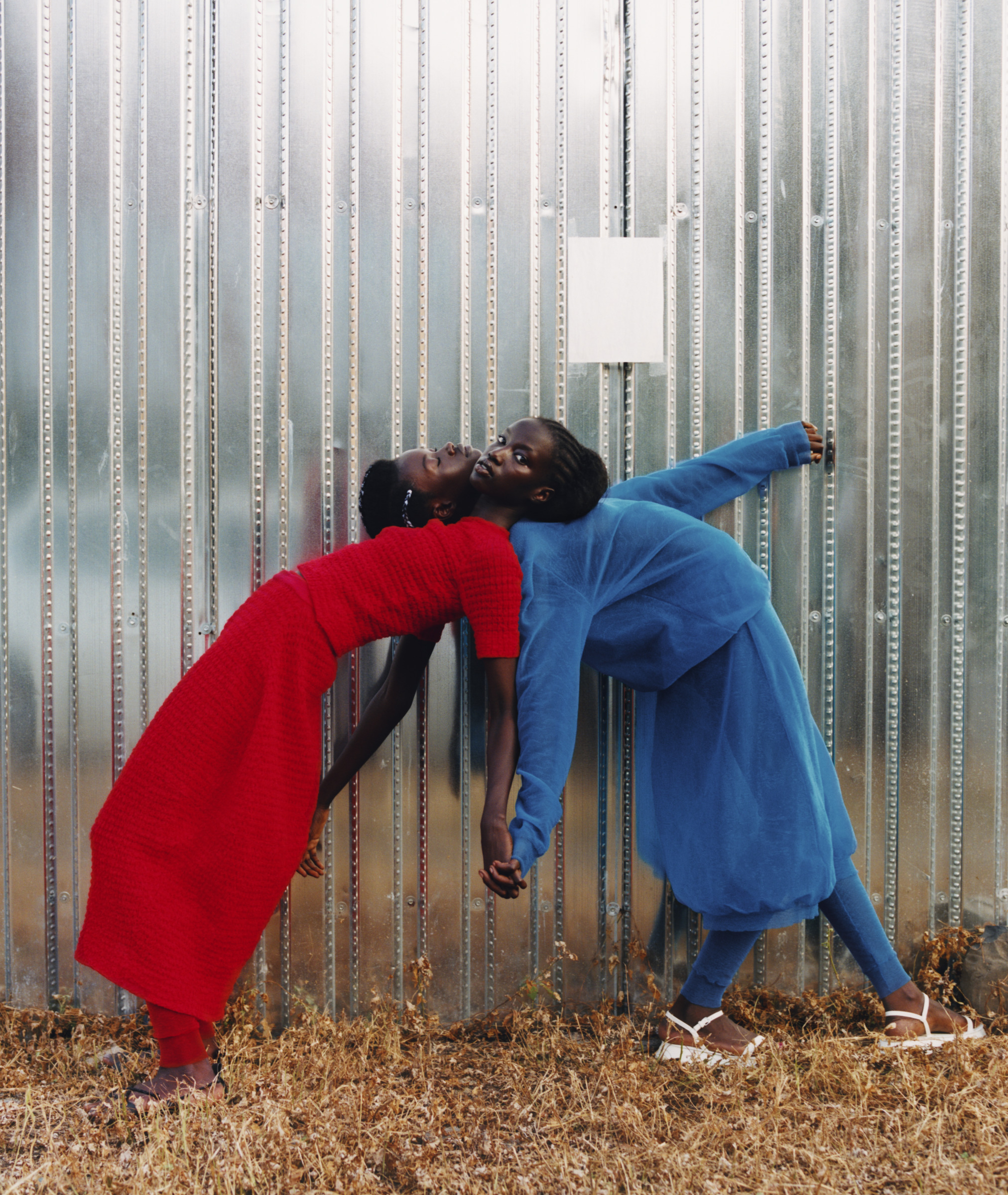 Two people, one dressed in bright red and the other in blue, lean on each other