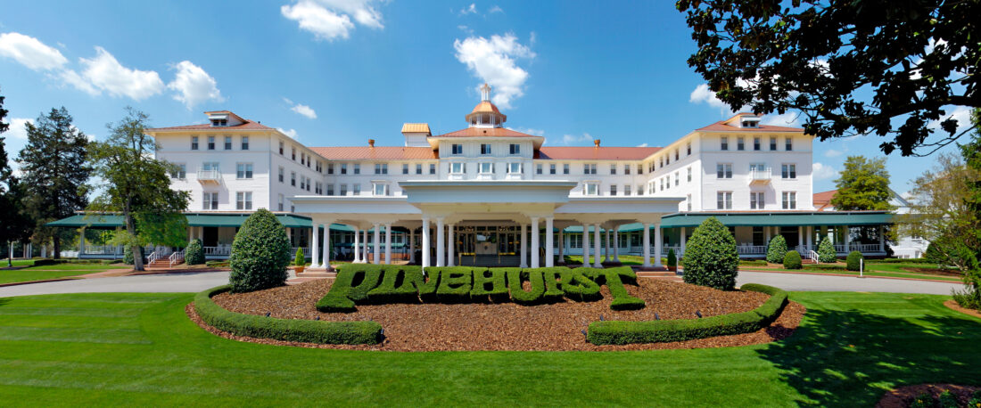 A large white building with red roof and hedges in front trimmed to spell out Pinehurst.