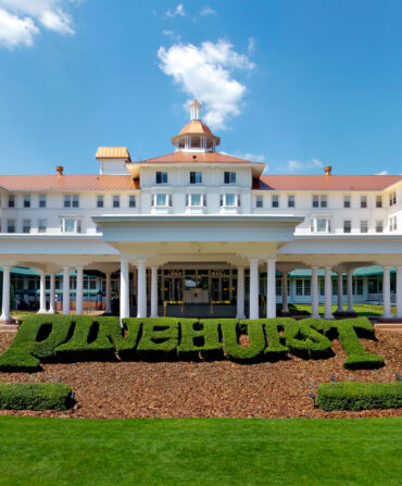 A large white building with red roof and hedges in front trimmed to spell out Pinehurst.