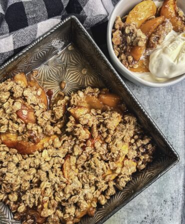 A peach crisp in a pan with a bowl of peach crisp and ice cream next to it