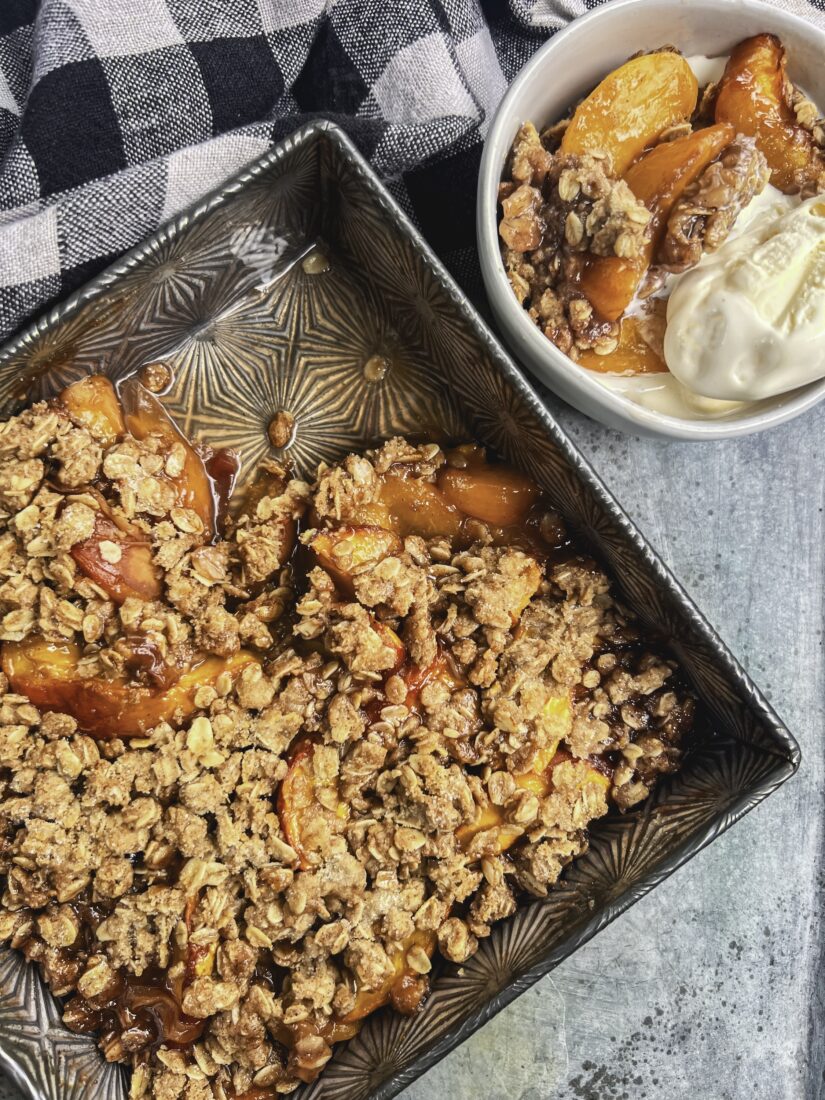 A peach crisp in a pan with a bowl of peach crisp and ice cream next to it