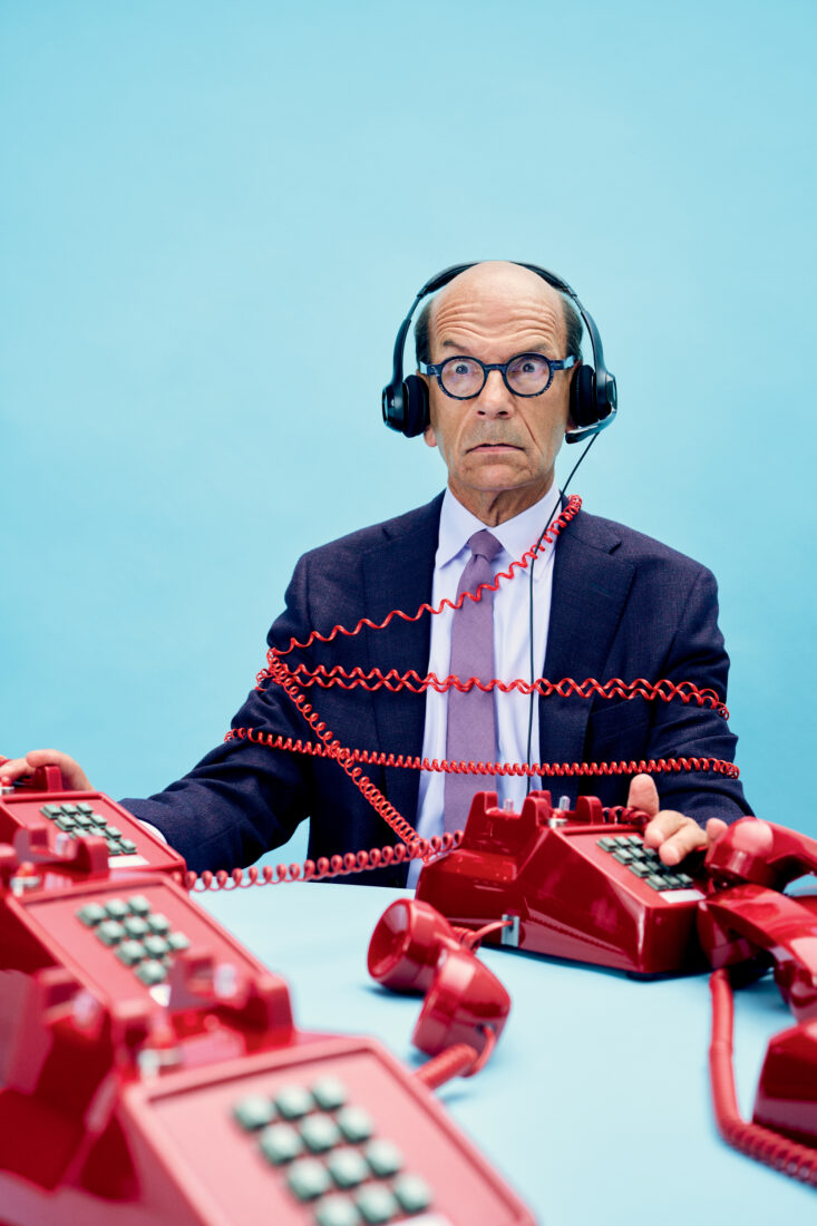 A man with headphones sits with red phone cords wrapped around him