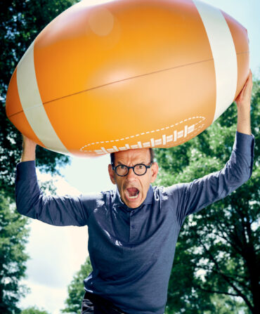 A man holds a giant football above his head with his mouth open in a yell