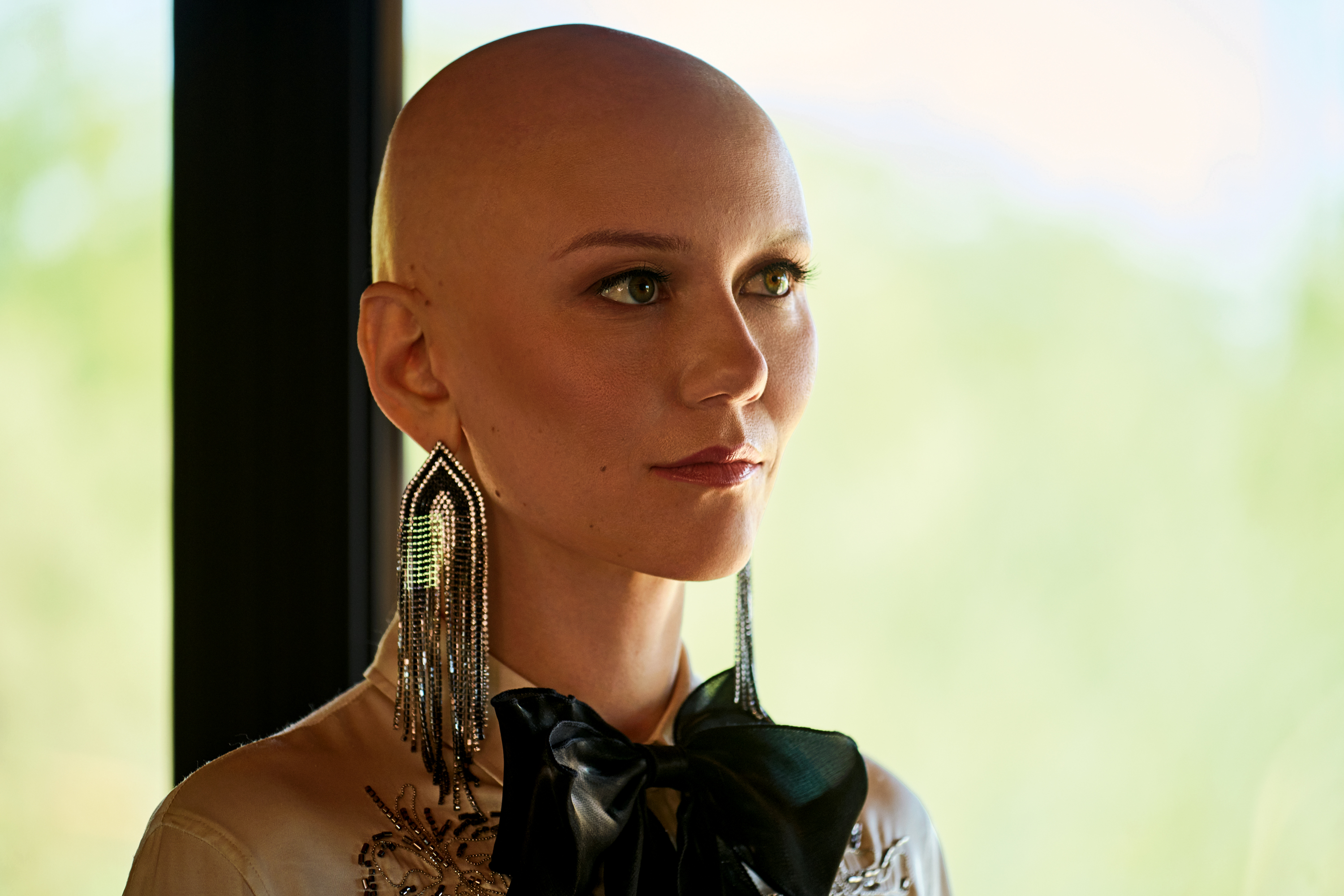 A portrait of a woman without hair on her head. She wears long, sparkly earrings.