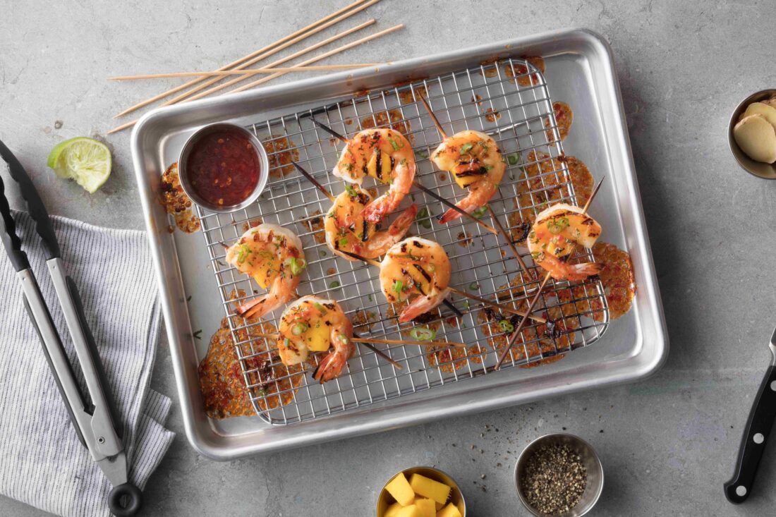 shrimp on skewers on a rack and baking sheet with tongs on a table