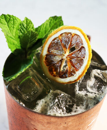 A cocktail in a copper cup, garnished with a lemon and mint