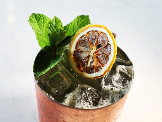 A cocktail in a copper cup, garnished with a lemon and mint