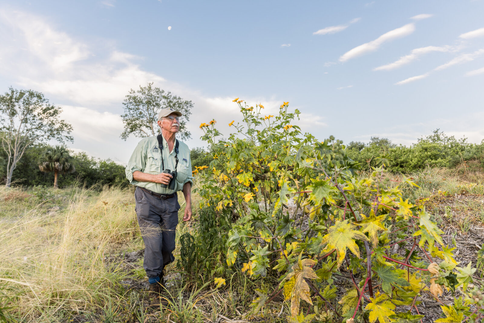 A man stands in a field with binoculars