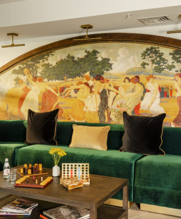 A lounge with a green velvet sofa and a mural