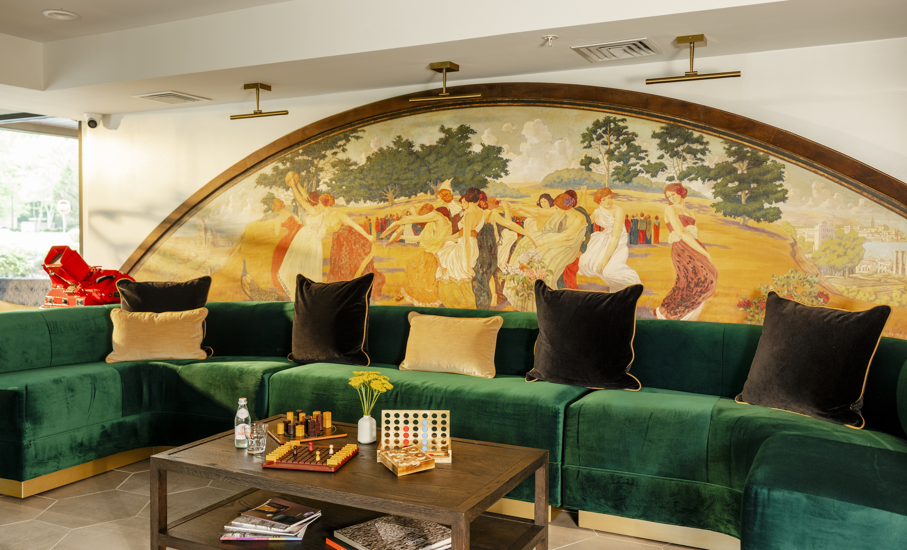 A lounge with a green velvet sofa and a mural