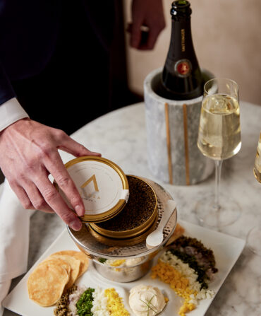 A hand pulls a lid off caviar at a set table