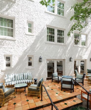 A white building with a terra cotta tile patio with blue furniture