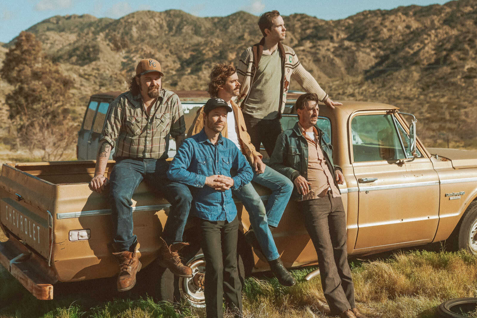 A group of men sit against a truck in a dessert