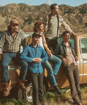 A group of men sit against a truck in a dessert