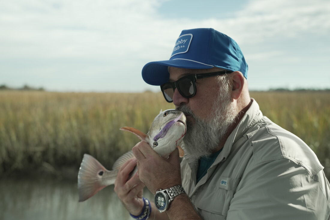 A man holds a fish in a marsh setting