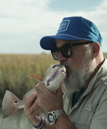 A man holds a fish in a marsh setting