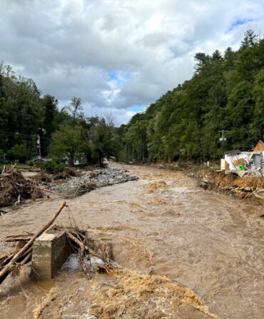 A destroyed road and structures with an overflowing brown river